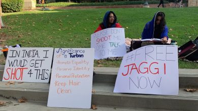 Two people sitting in grass. Posters in front of them that say: "In India, I would get shot 4 this", "significance of a turban: promote equality, perserve identity, personal protection, keep hair clean"; "please don't shoot me, come talk to me"; and "free JAGGI now"