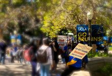 Several students and UC-AFT members gather on Bruin Walk. One UC-AFT member, wearing a blue t-shirt, is holding a picket sign that says, “UC-AFT Faculty Demand Job Security.” Another UC-AFT member wearing a blue t-shirt is holding a picket sign that says, “End Unpaid Work Now!” Near the two picket signs is a UCLA post lamp banner that says, “Welcome to UCLA GO BRUINS!” About six students are standing around the two UC-AFT members. Other students and UC-AFT members are blurred in the background.