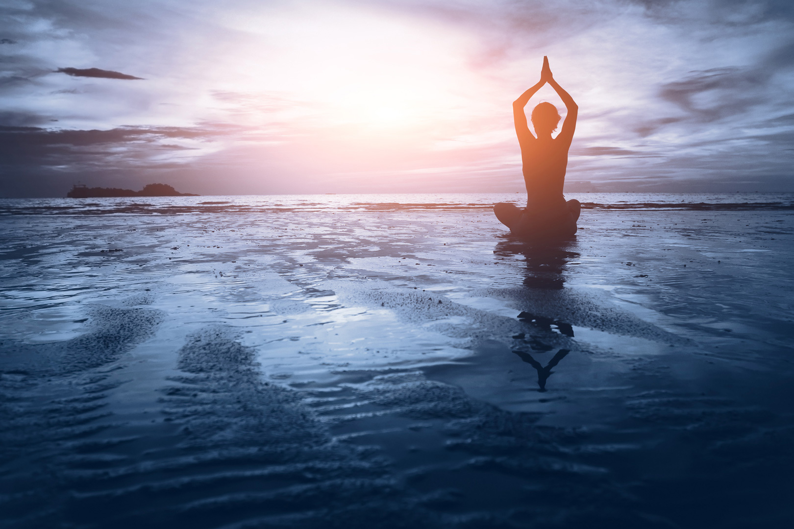 A person holding a tree pose while sitting down on a beach