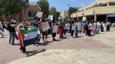 Image Description: A crowd of protesters gathers in Bruin Plaza. On the right, a protester holds up a Palestinian flag. Many protesters hold signs — some of which read “Divest, PPL > Profit,” “UC Divest,” and “FUND STUDENTS NOT WAR.”